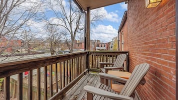 A wooden deck with a brick wall, two Adirondack chairs, and a table.