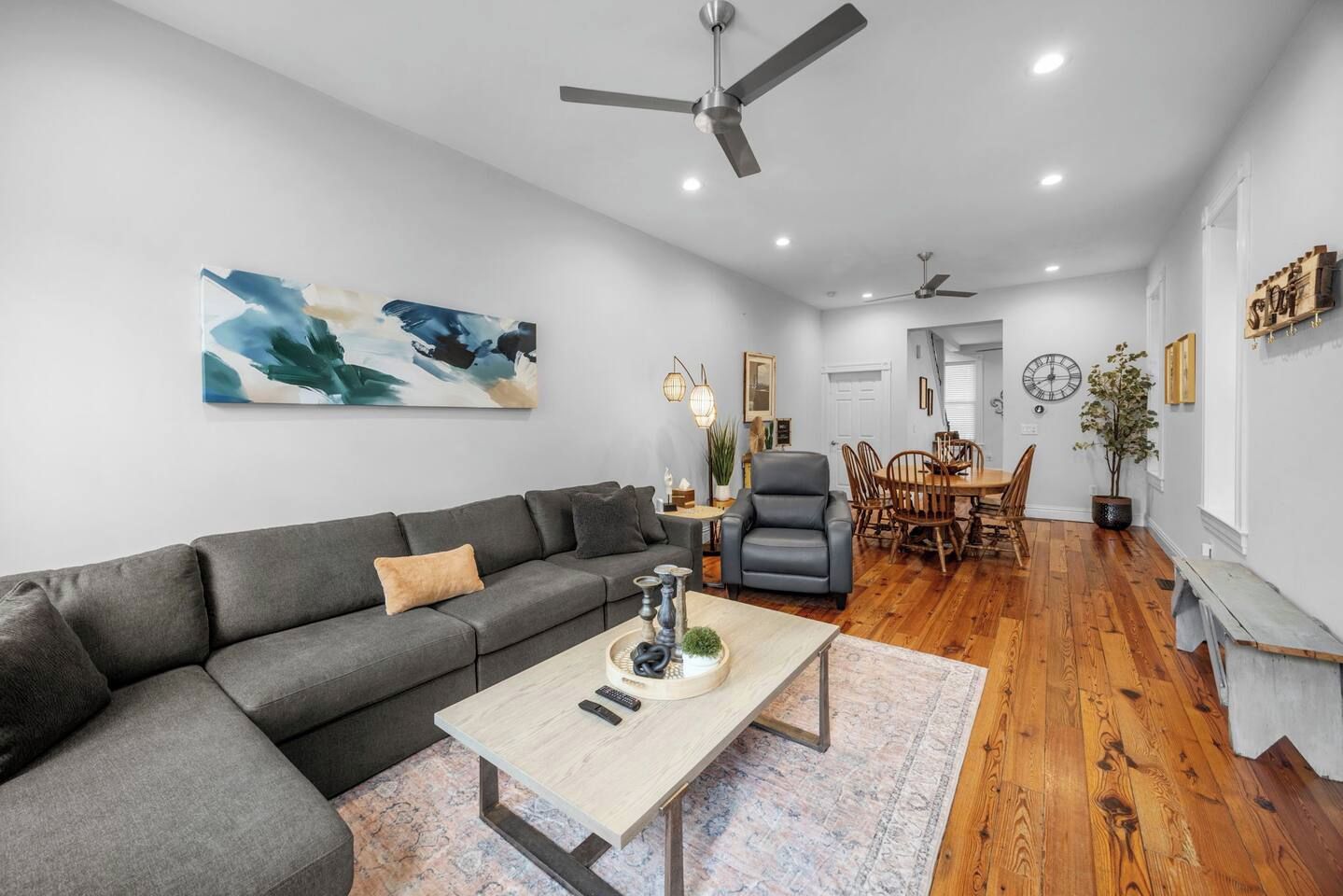 A modern living room with a grey sofa, a wooden dining table, and a ceiling fan.