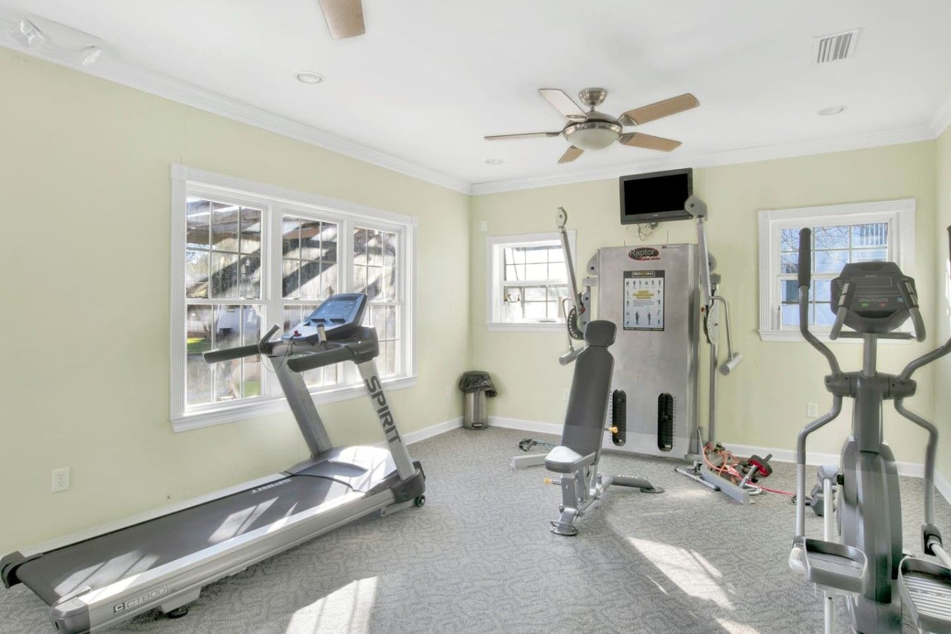 A home gym with a treadmill, elliptical, and weight machine.