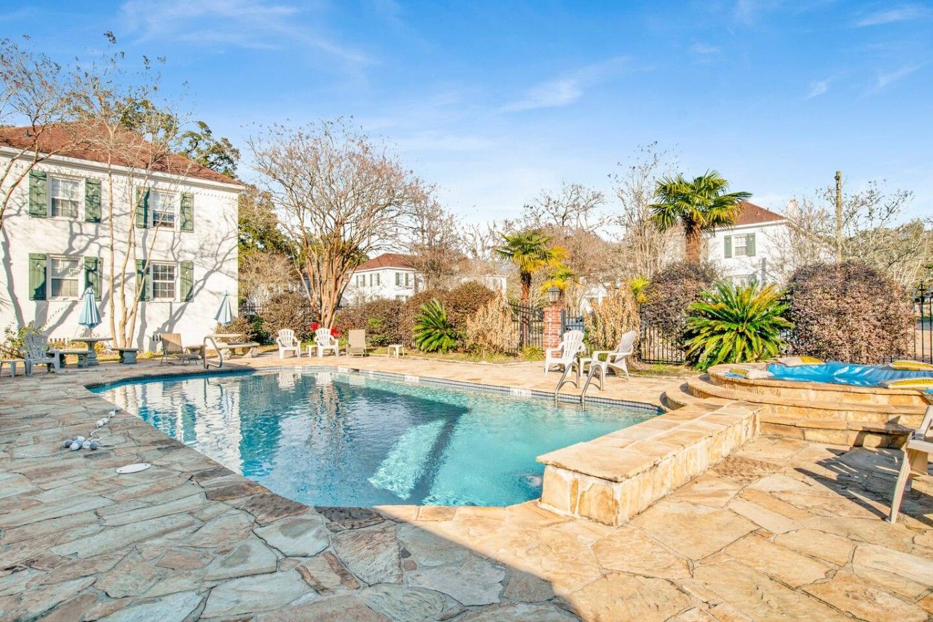 A swimming pool with stone tiles, surrounded by outdoor furniture and trees.