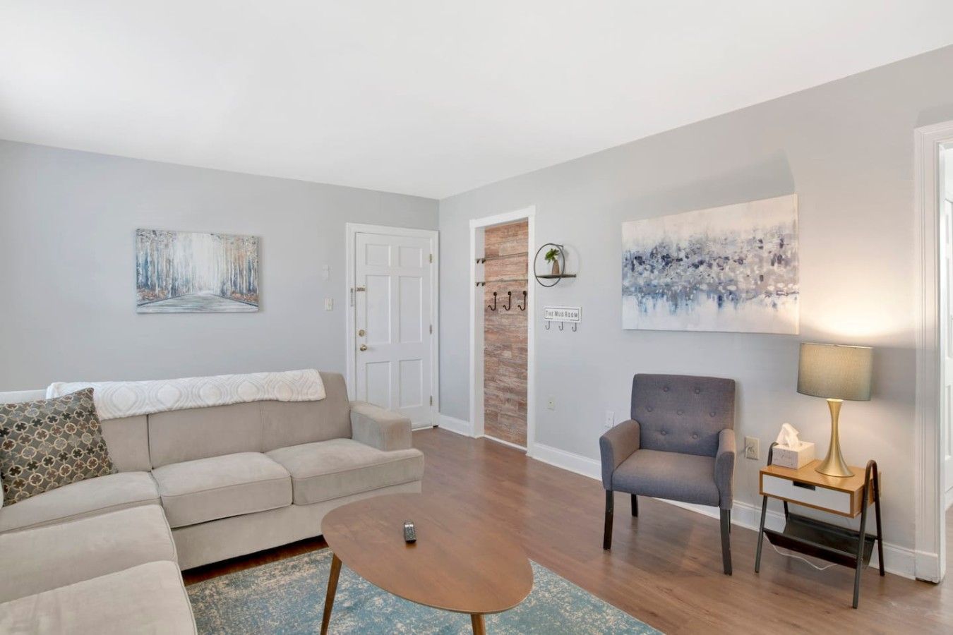 A living room with a sofa, armchair, coffee table, and artwork on the walls.