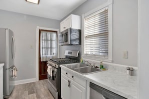 A modern kitchen with stainless steel appliances, a marble countertop, and a window with blinds. - Southern Comfort (Mobile)