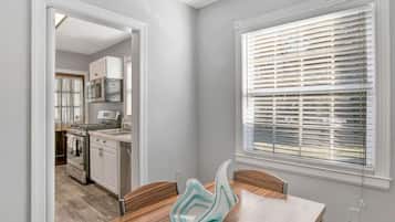 A modern kitchen with a dining area, featuring a large window with blinds, a wooden dining table, and a kitchen island.
