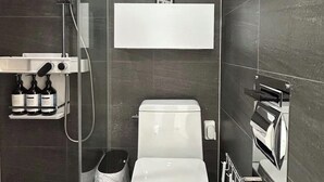 Un baño moderno con inodoro, ducha y un estante con artículos de aseo.