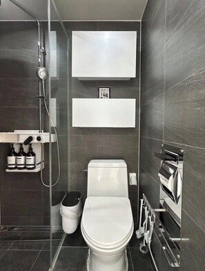 Ein modernes Badezimmer mit Toilette, Dusche und Ablage für Pflegeprodukte.