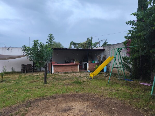 A backyard with a brick patio, a yellow slide, and a green swing set.