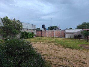 A fenced outdoor area with a grassy field, a brick wall, and a water tank.