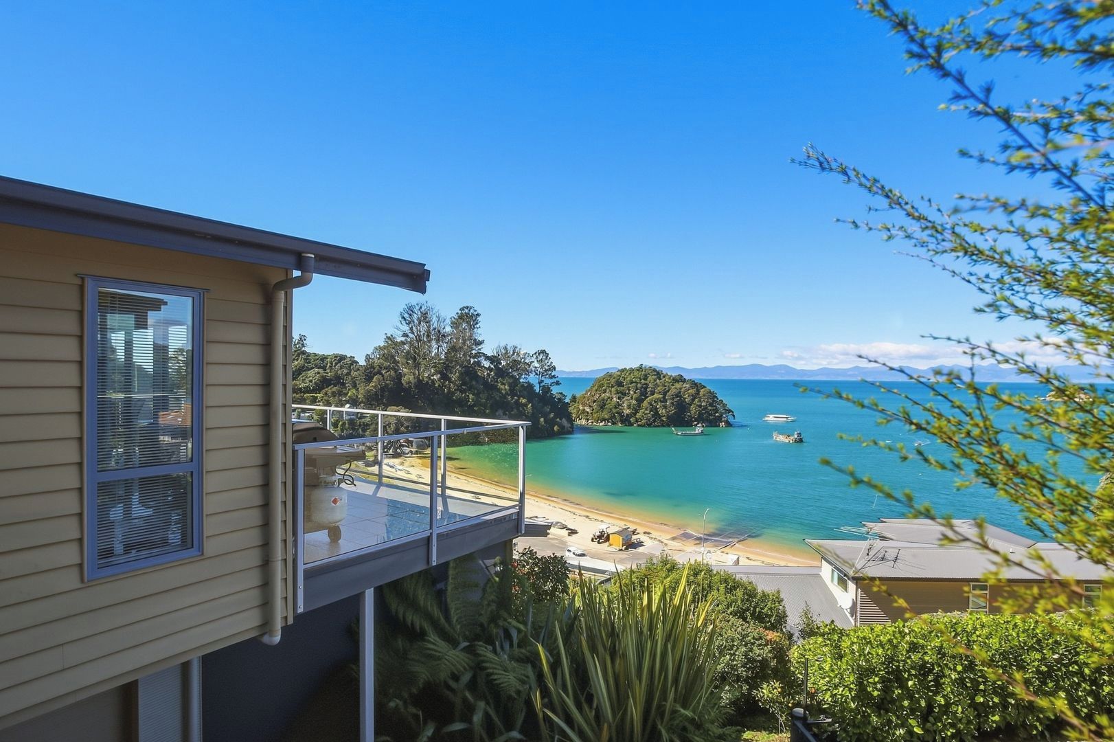 A residential property with a balcony overlooking a clear blue sea, a small island, and a beach.