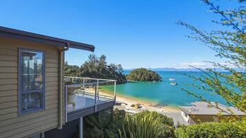 A residential property with a balcony overlooking a clear blue sea, a small island, and a beach.