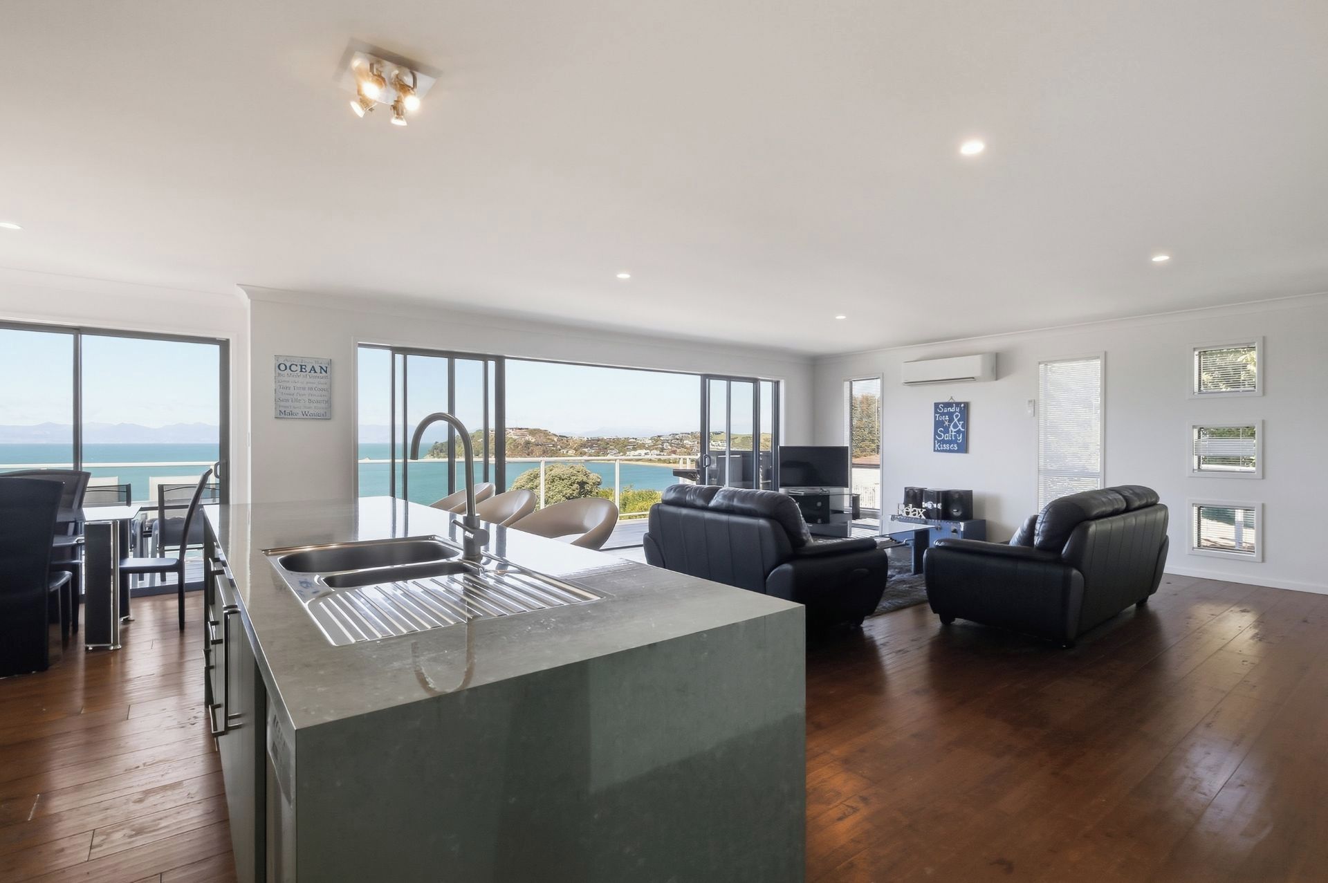 A modern kitchen with a large island, a dining area with chairs, and a view of the sea.
