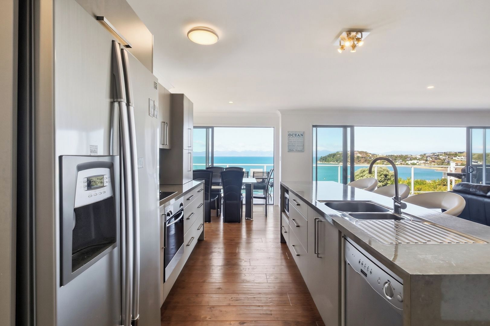 A modern kitchen with stainless steel appliances, a wooden floor, and a view of the ocean.