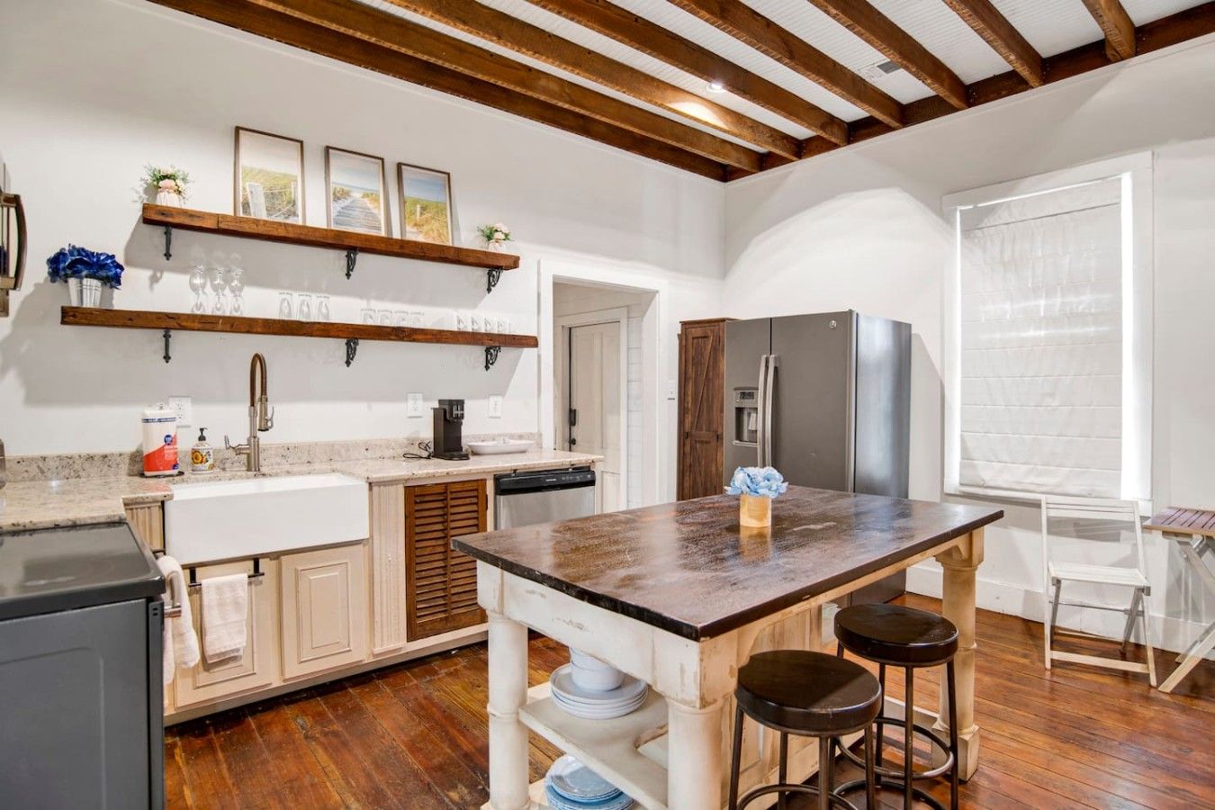 Cozinha com ilha central, banquetas, geladeira e janela com persianas.