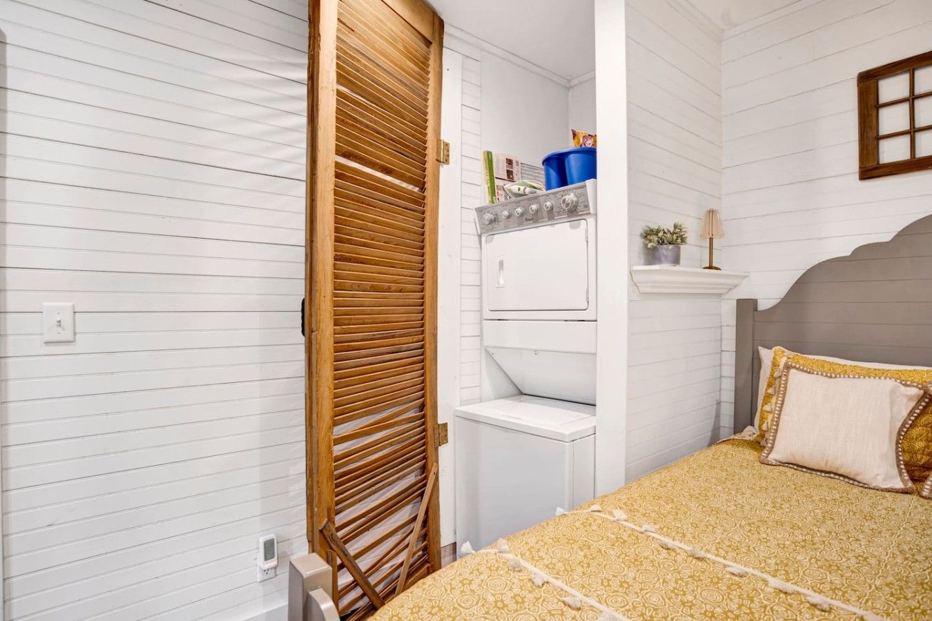 Quarto compacto com cama, máquina de lavar e porta de madeira.