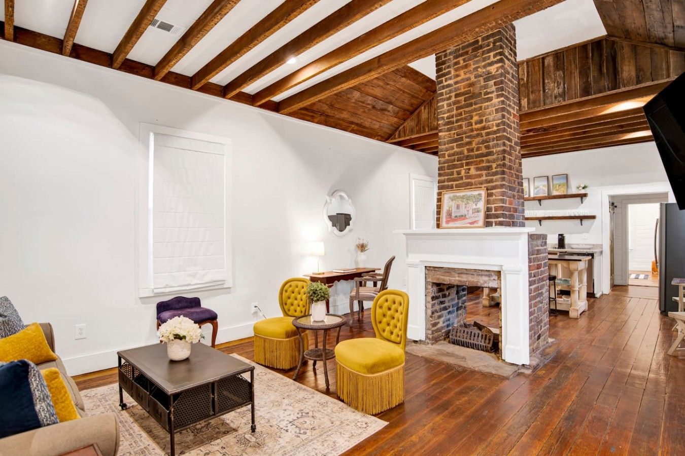 A spacious living room with a fireplace, wooden beams, and a dining area.