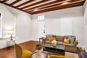 A living room with a sofa, coffee table, and a lamp. There is a door and a window with blinds. - Saint Michaels Haven (Mobile)