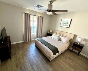 A bedroom with a bed, a ceiling fan, a nightstand, a dresser, and a window with curtains.