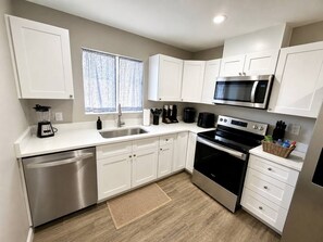 A modern kitchen with white cabinets, stainless steel appliances, and a window with patterned curtains.