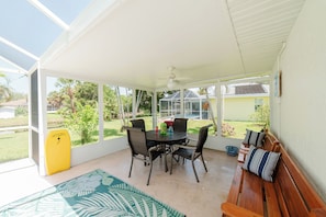 A covered patio area with a table and chairs, a bench, and a yellow surfboard. - Waterfront heated pool home near beaches. 2 bedroom suites! (Port Charlotte)