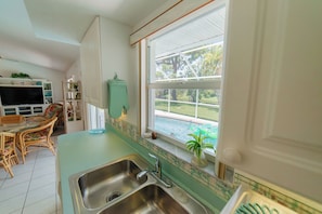 A kitchen with a large window, a sink, and a dining area with a table and chairs. - Waterfront heated pool home near beaches. 2 bedroom suites! (Port Charlotte)