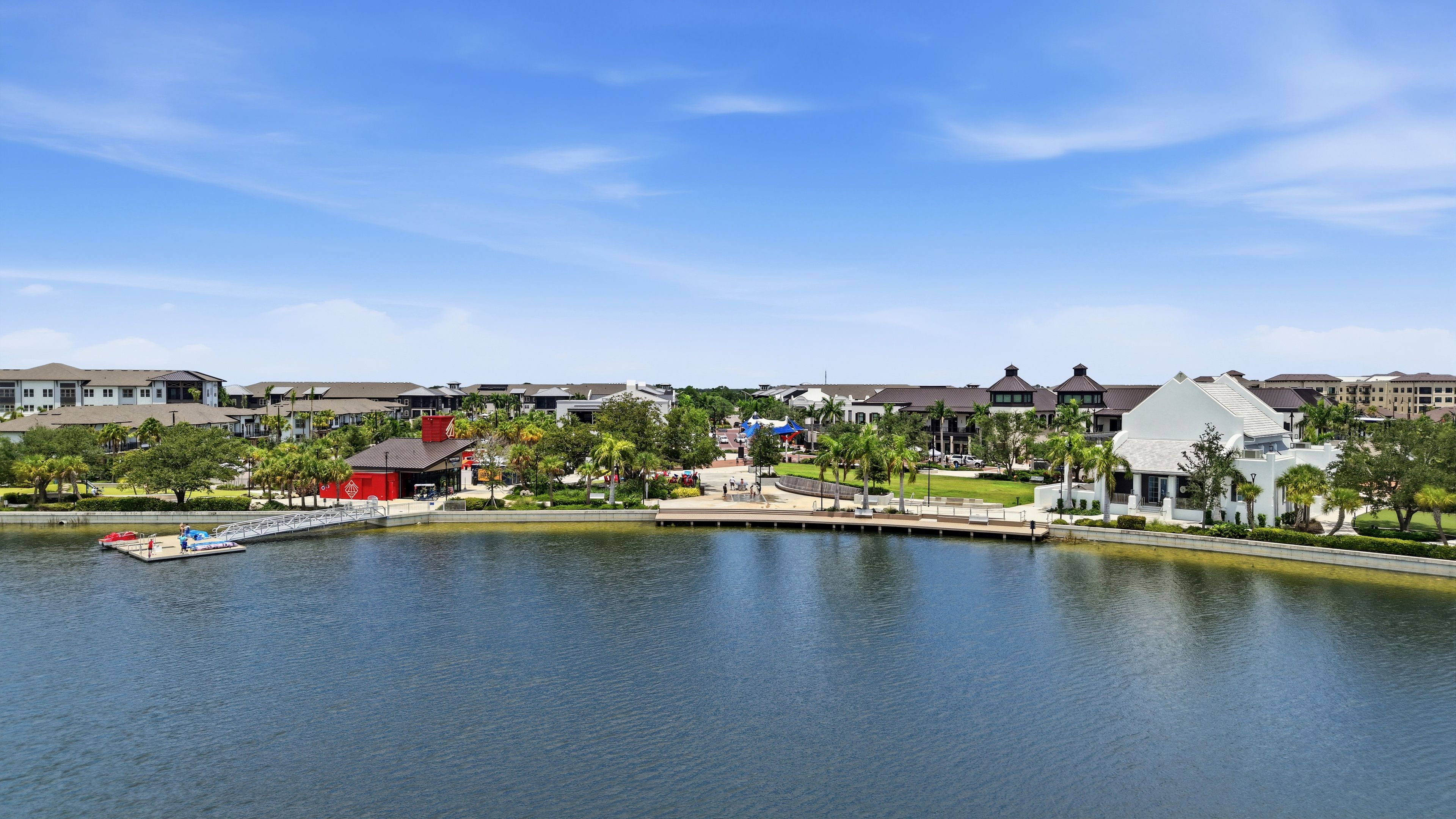 A lakeside view of a residential area with houses, a dock, and a small building with a red roof.