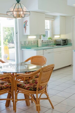 A kitchen with a glass dining table surrounded by wicker chairs, a microwave, and a window with a view of greenery. - Waterfront heated pool home near beaches. 2 bedroom suites! (Port Charlotte)