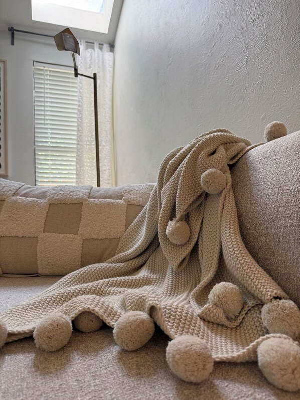 A cozy room with a knitted throw blanket draped over a couch, a window with blinds, and a floor lamp.