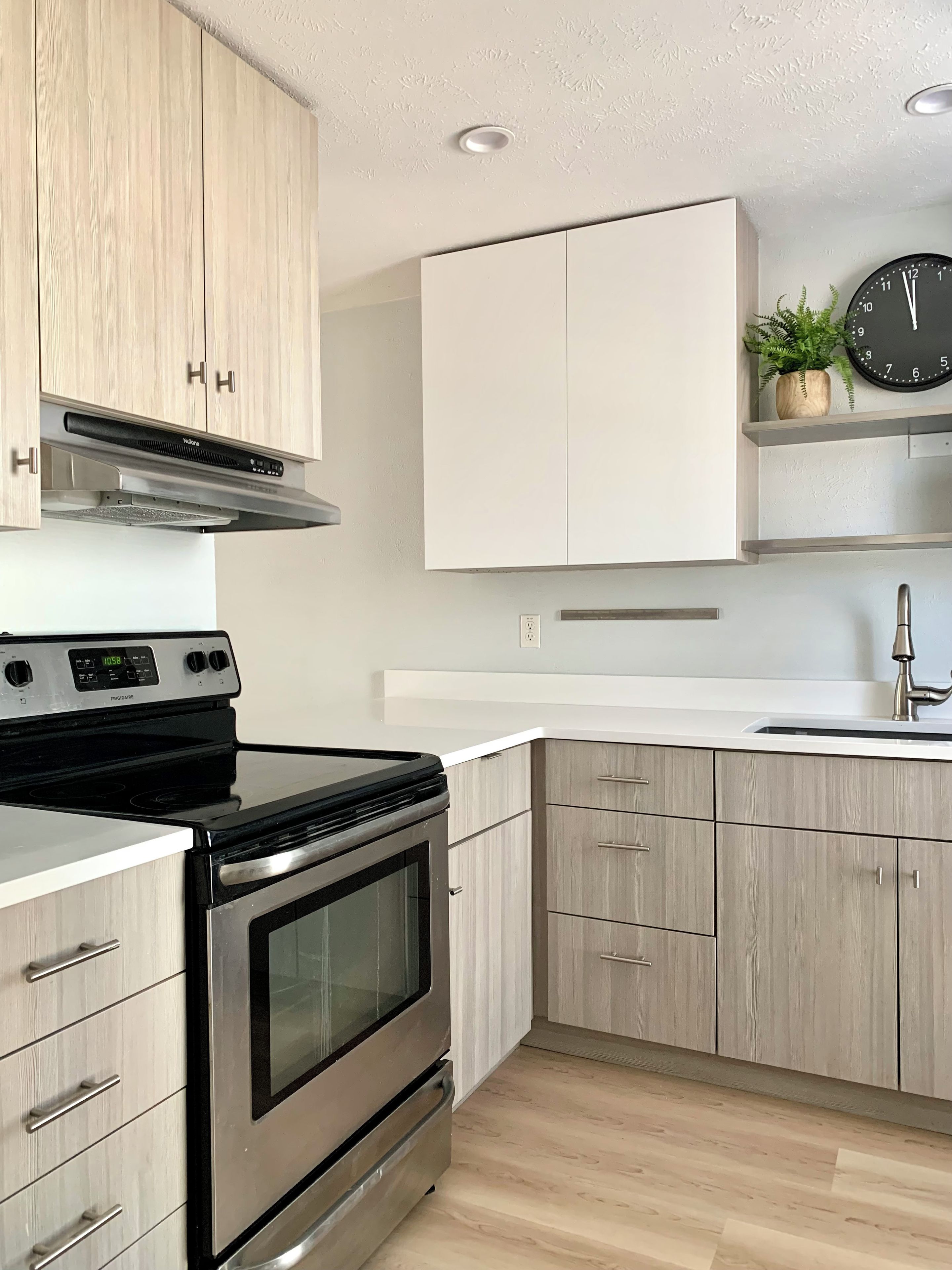 A modern kitchen with stainless steel appliances, light wood cabinetry, and a built-in oven.