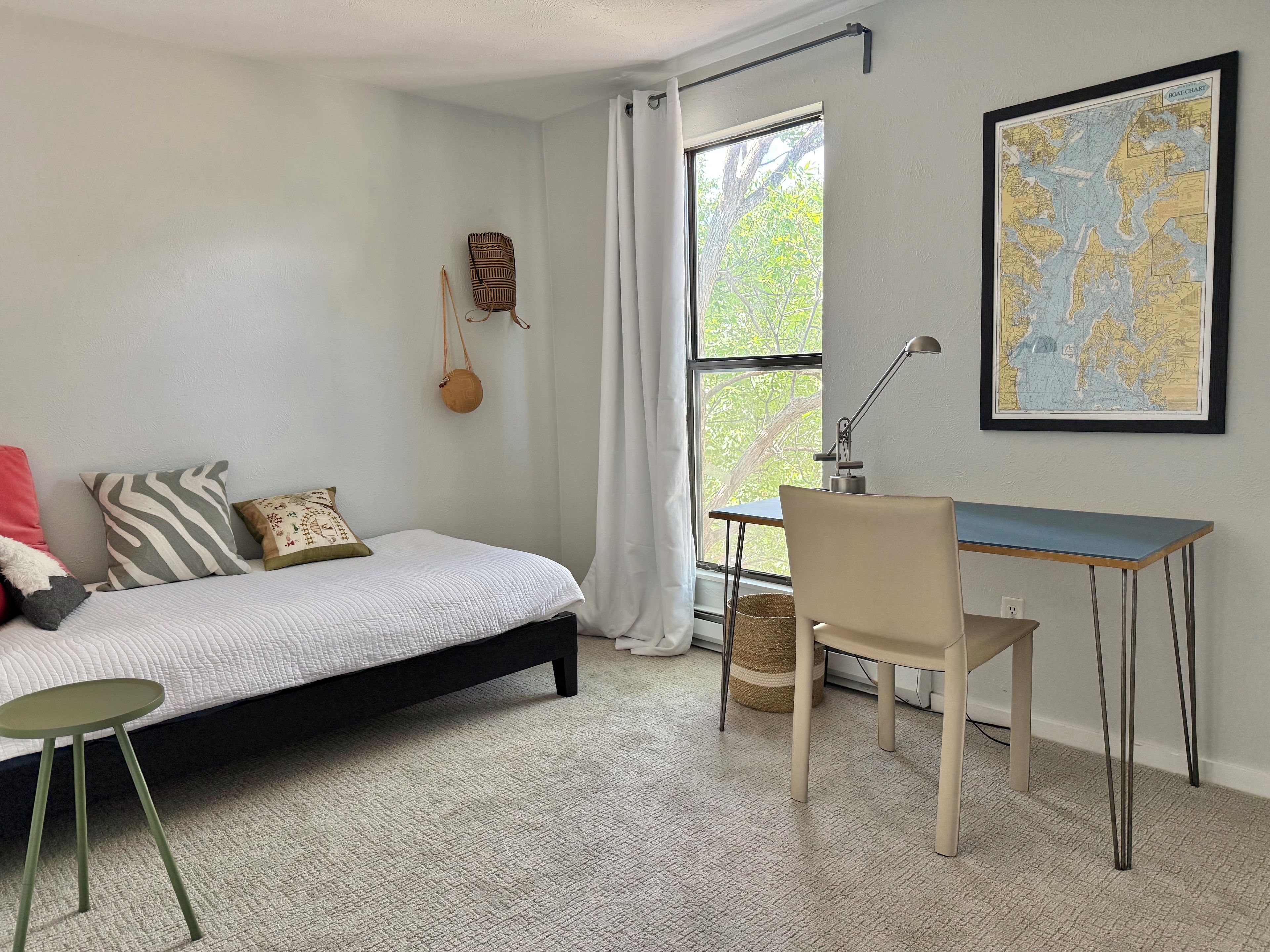 A bedroom with a bed, a desk, a chair, a map on the wall, and a window with curtains.