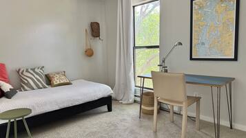 A bedroom with a bed, a desk, a chair, a map on the wall, and a window with curtains.