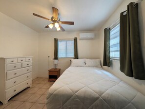 A bedroom with a bed, a dresser, a nightstand, a ceiling fan, and a window with curtains. - Charming 2BR Tucson Home – Minutes to U of A & Downtown! (Tucson)