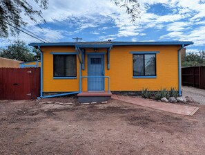 A two-story yellow building with a blue door and windows, a small porch, and a fenced yard. - Charming 2BR Tucson Home – Minutes to U of A & Downtown! (Tucson)