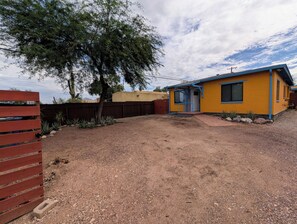 A residential property with a fenced yard, a single-story house with a blue door, and a large tree. - Charming 2BR Tucson Home – Minutes to U of A & Downtown! (Tucson)
