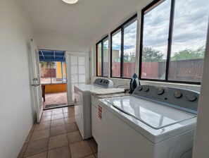 A laundry room with a front-loading washer and dryer, a window with a view of the backyard, and a door leading to an outdoor area. - Charming 2BR Tucson Home – Minutes to U of A & Downtown! (Tucson)