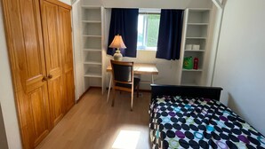 A bedroom with a wooden wardrobe, a desk with a chair, a bed with a polka dot bedspread, and built-in shelving. - Room-pretty Room -shared Accommodation (Coquitlam)