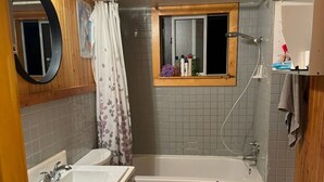 A bathroom with wooden paneling, a bathtub, a toilet, two sinks, and a window with a showerhead. - Room-pretty Room -shared Accommodation (Coquitlam)