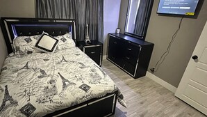 Ein Schlafzimmer mit Bett, Nachttisch, Schminktisch, Deckenventilator, Fernseher und einer Tür.