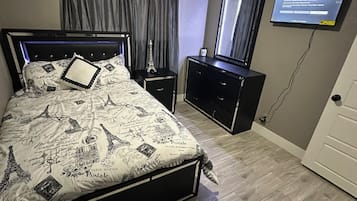 A bedroom with a bed, a nightstand, a dresser, a ceiling fan, a television, and a door.