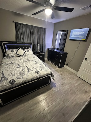 A bedroom with a bed, a nightstand, a dresser, a ceiling fan, a television, and a door. - Beautiful Spacious and remodeled 4-bedroom house in  san antonio! (San Antonio)