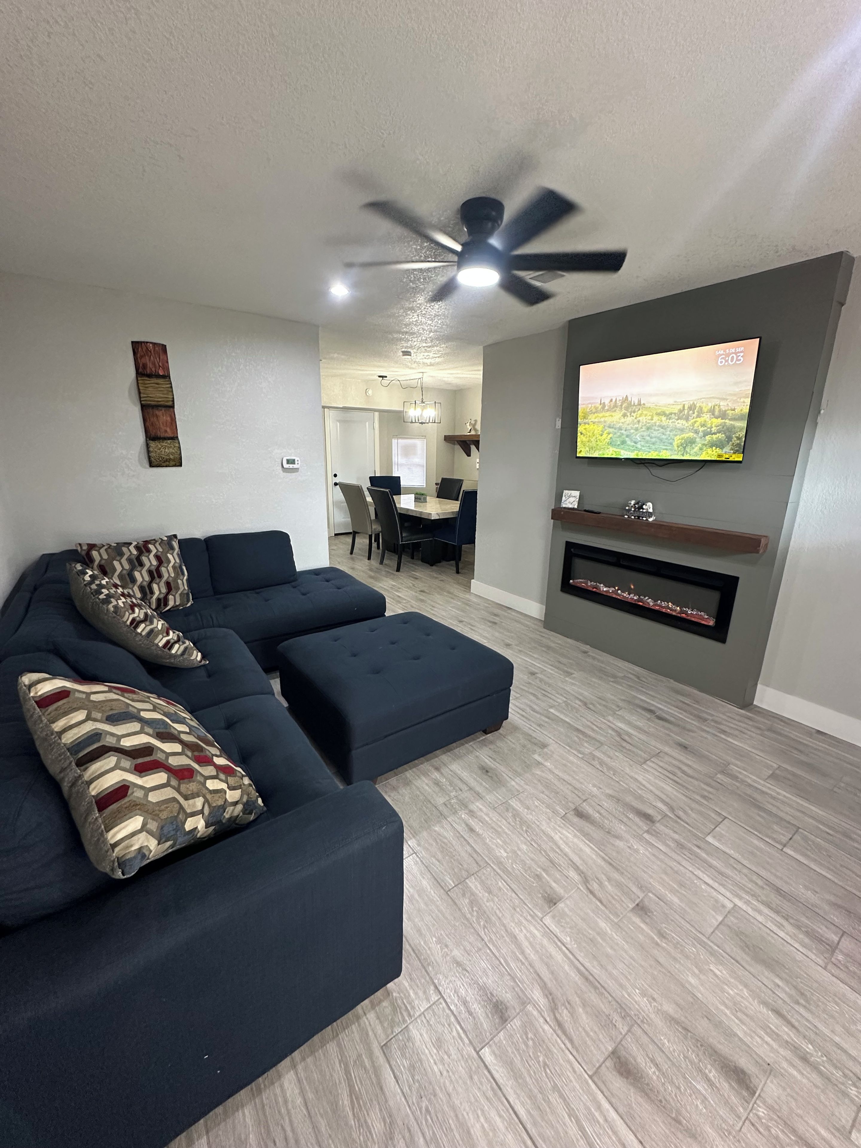 A modern living room with a sectional sofa, a flat-screen TV, and a ceiling fan.