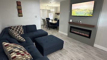 A modern living room with a sectional sofa, a flat-screen TV, and a ceiling fan.