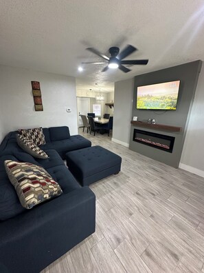 Uma sala de estar moderna com sofá seccional, TV de tela plana e ventilador de teto.