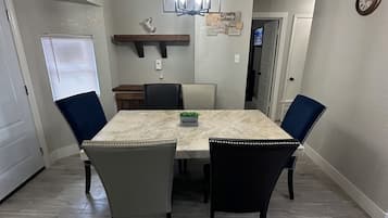 A dining area with a marble table, four chairs, a chandelier, and a clock on the wall.