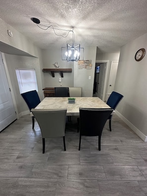 A dining area with a marble table, four chairs, a chandelier, and a clock on the wall. - Beautiful Spacious and remodeled 4-bedroom house in  san antonio! (San Antonio)