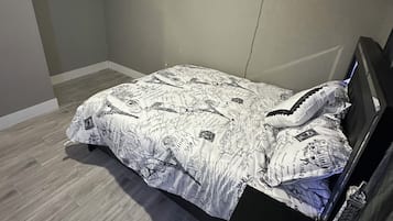Un dormitori amb un llit, un ventilador de sostre, una prestatgeria penjada a la paret amb sabates i una fotografia petita.