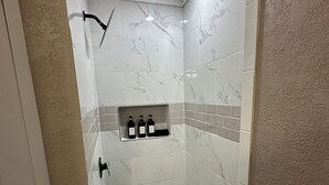 Eine Dusche mit weißen Marmorfliesen, ein Ablagefach für Toilettenartikel und ein Mosaikboden.