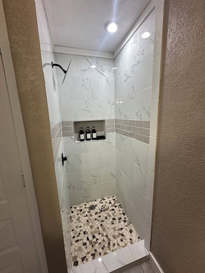 A shower with white marble tiles, a shelf with toiletries, and a mosaic floor. - Beautiful Spacious and remodeled 4-bedroom house in  san antonio! (San Antonio)
