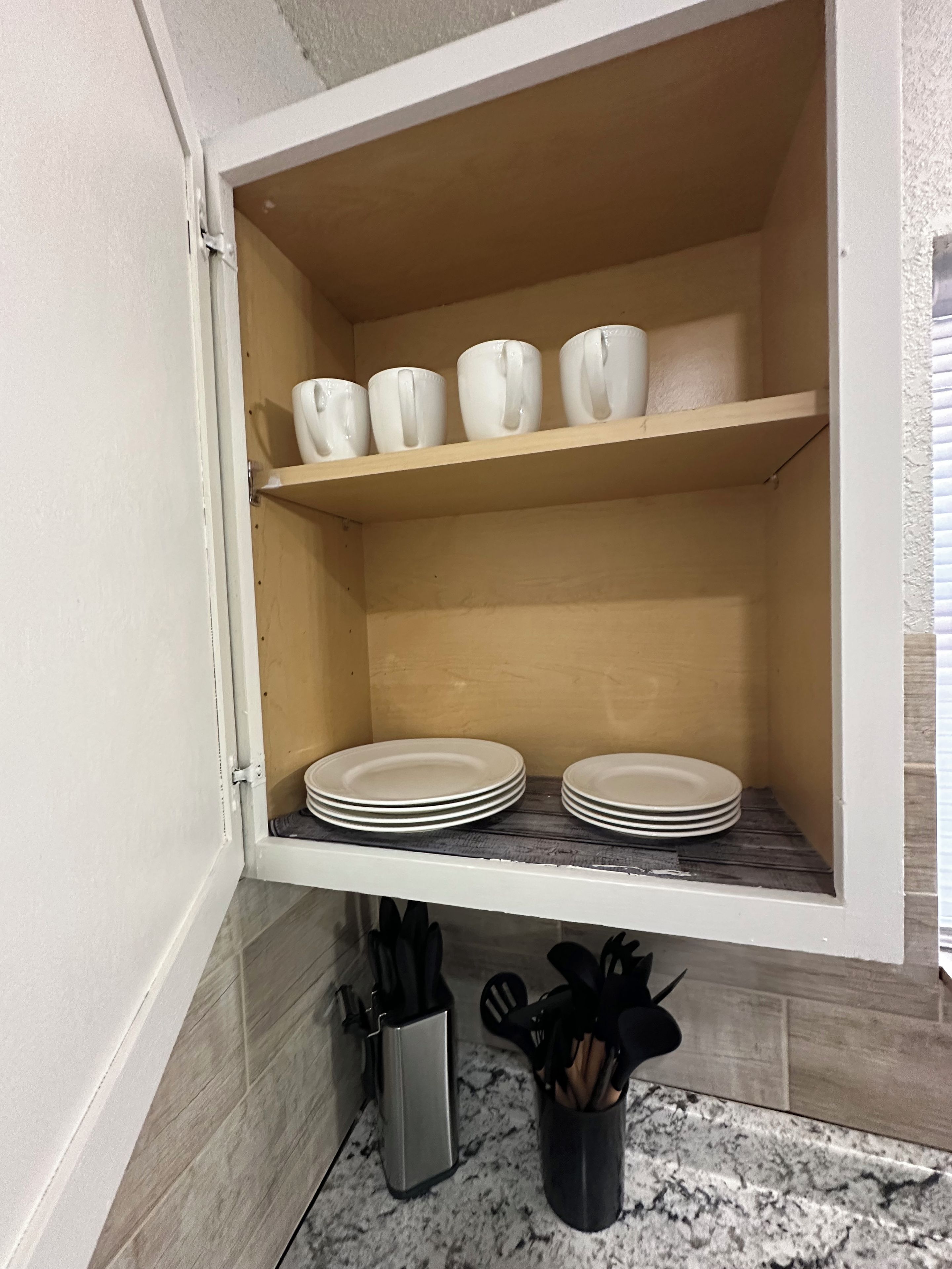 Un armari de cuina amb tasses i plats blancs, un suport per ganivets i un colador d'estris.