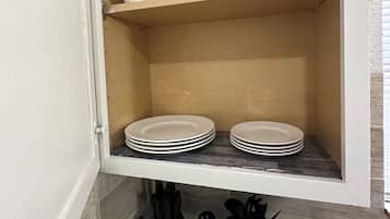 Un armari de cuina amb tasses i plats blancs, un suport per ganivets i un colador d'estris.