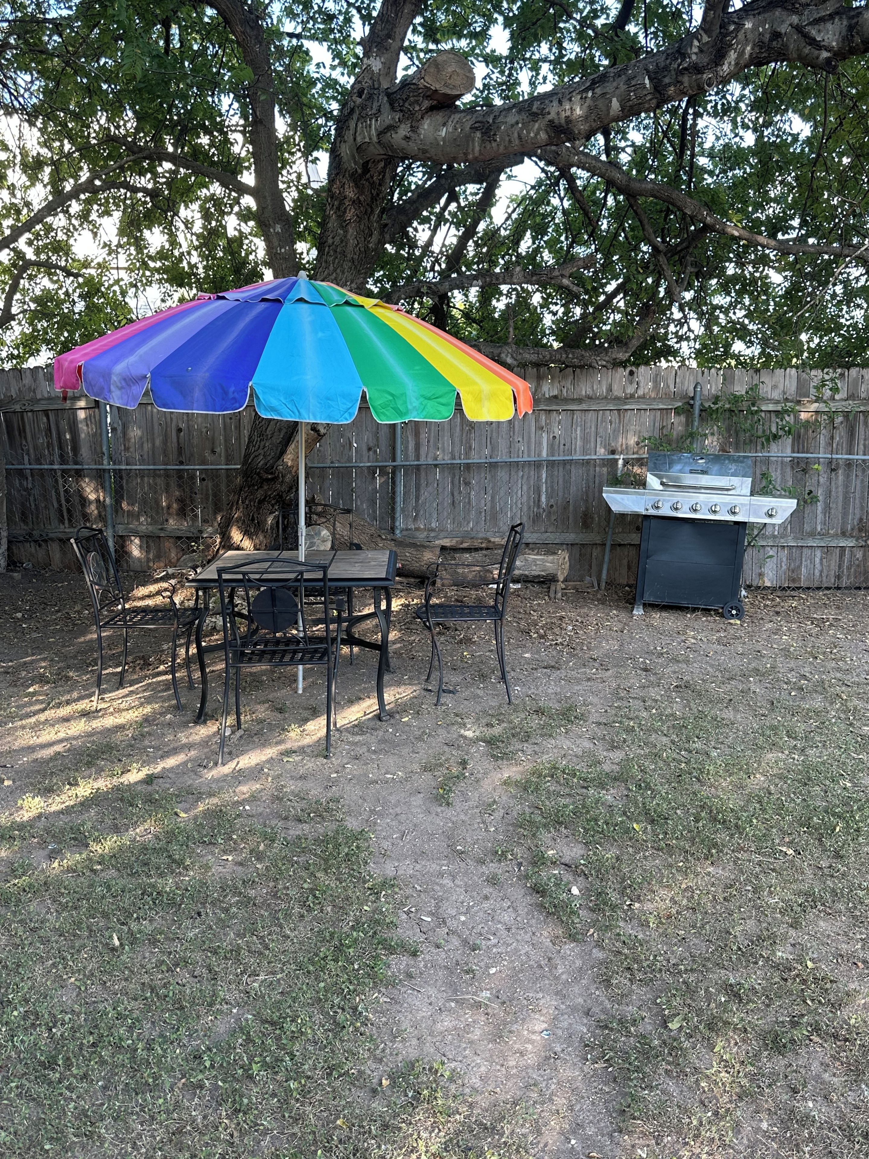 An outdoor dining area with a table and chairs, a barbecue grill, and a colorful umbrella.