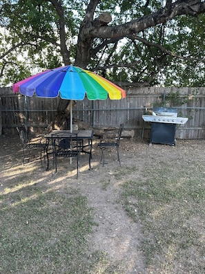 An outdoor dining area with a table and chairs, a barbecue grill, and a colorful umbrella. - Beautiful Spacious and remodeled 4-bedroom house in  san antonio! (San Antonio)